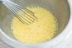 a mixing bowl filled with yellow liquid and whisk