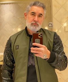 a man taking a selfie with his cell phone in front of him and wearing a green jacket