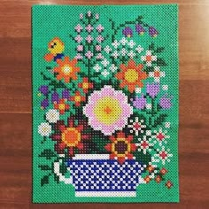 a cross stitch picture with flowers in a blue vase on a wooden table next to a green background