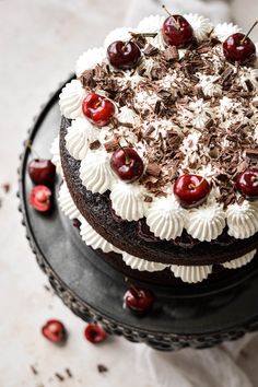 a chocolate cake topped with cherries and white frosting on top of a black plate