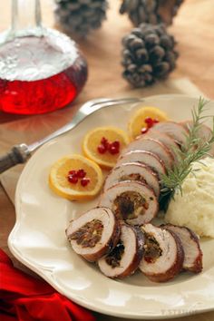 a white plate topped with sliced meat and mashed potatoes next to orange slices on a wooden table