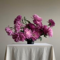 a black vase filled with purple flowers on top of a white tablecloth covered table