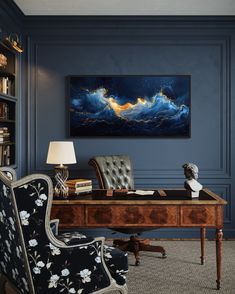 an office with blue walls and a large painting on the wall above it's desk