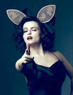 a woman in a black dress and bunny ears pointing at something with her finger to the side