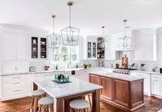 a large kitchen with white cabinets and marble counter tops, two stools at the island