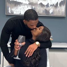 a man and woman kissing each other while holding a wine glass in front of them