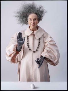 an older woman with grey hair wearing gloves and holding her hands out to the side