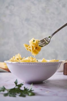 a bowl filled with pasta being held by a fork over the top of it and topped with parmesan cheese