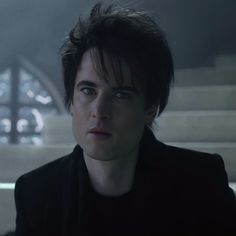 a young man with dark hair stares into the distance while sitting in front of stairs