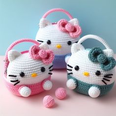 three crocheted hello kitty purses on a pink surface next to some balls