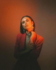 a woman standing in front of a red wall with her hands on her chest and looking off to the side