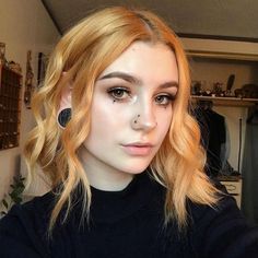 a woman with blonde hair and black eyeliner is looking at the camera while wearing ear piercings