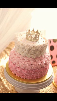 a pink and white cake with a crown on top sitting on a gold platter