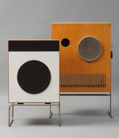 two different types of speakers sitting next to each other on metal stands with wood panels