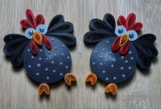 two black roosters made out of paper on a wooden table with blue eyes and orange tails