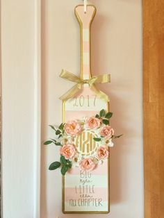 a pink and gold door hanger with flowers on it, hanging from the wall