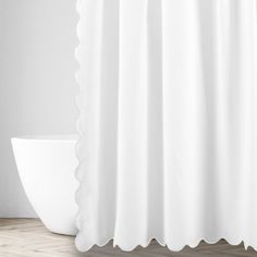 a white shower curtain next to a toilet in a room with hardwood floors and walls