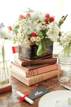 a stack of books sitting on top of a wooden table next to a vase filled with flowers