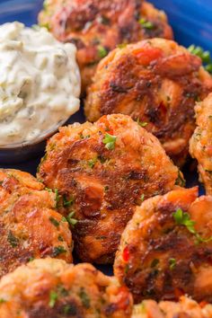 several crab cakes on a blue plate with a small bowl of dip