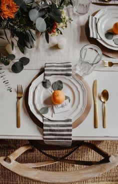 a place setting with oranges and greenery on the table, along with silverware