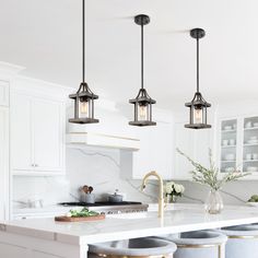 three lights hanging over a kitchen island with stools and counter tops in front of it