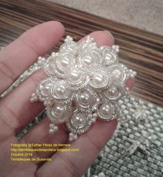 a hand holding a white brooch with pearls on it's center and filigrees in the middle