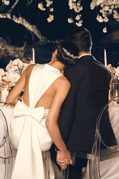 a man and woman sitting at a table with white flowers on it, facing each other