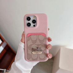 a woman holding up her pink coach phone case