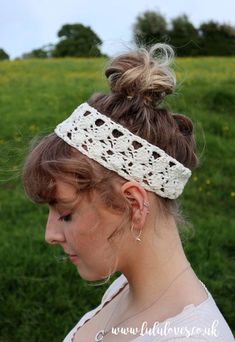 a woman wearing a crochet headband in front of a grassy field with yellow flowers