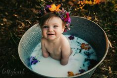 a baby sitting in a bucket full of milk with flowers on her head and smiling