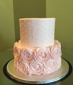 a three tiered cake with white frosting and pink roses on top is sitting on a table