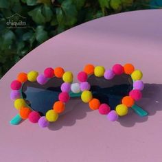 a pair of heart shaped sunglasses with pom - poms on the lens, sitting on top of a pink table