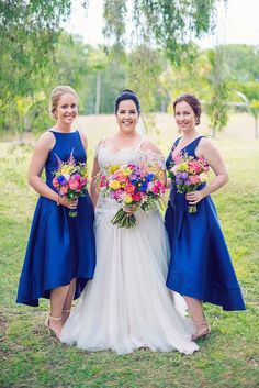 three bridesmaids in blue dresses posing for the camera with their bouquets on