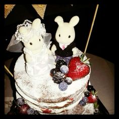 a wedding cake with two bunnies on top and berries in the shape of rabbits