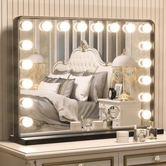 a white bed sitting under a large mirror with lights on it's sides next to a night stand