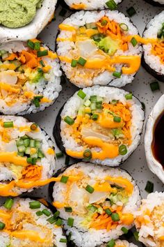 sushi with sauce and green onions on a white platter next to dipping sauce