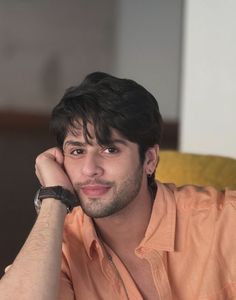 a man sitting down with his hand on his chin and looking at the camera while wearing an orange shirt