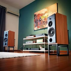 two speakers sitting on top of a wooden shelf in front of a wall mounted painting