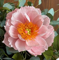 a large pink flower sitting on top of a wooden table next to green leaves and flowers