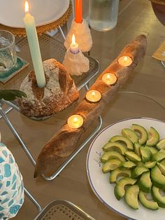 a table topped with bread and sliced cucumbers next to candles on top of plates