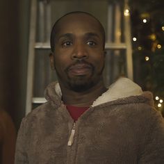 a man in a brown jacket standing next to a christmas tree