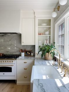 a kitchen with marble counter tops and white cabinets, along with brass pulls on the faucets