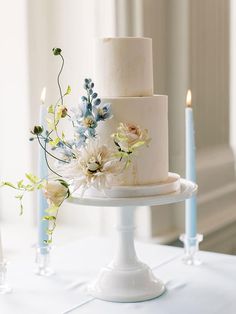 a three tiered cake with flowers and candles on the table in front of it