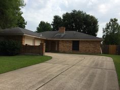 a house that is in the middle of a driveway with grass and trees around it