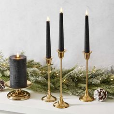 three candles are sitting on a mantle with pine cones and evergreen branches in the background