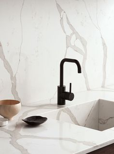 a white marble counter top with a black faucet and wooden bowl next to it