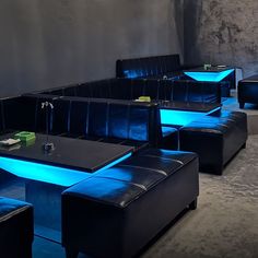 an empty restaurant with black leather couches and blue lights on the back wall,