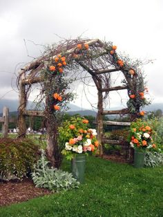 an arch made out of branches with flowers in buckets