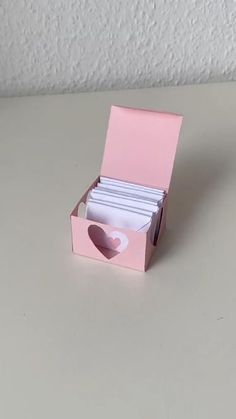 an open pink box with white cards in it on a table next to a cup