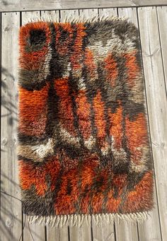 an orange and gray rug on a wooden floor with wood planks in the background